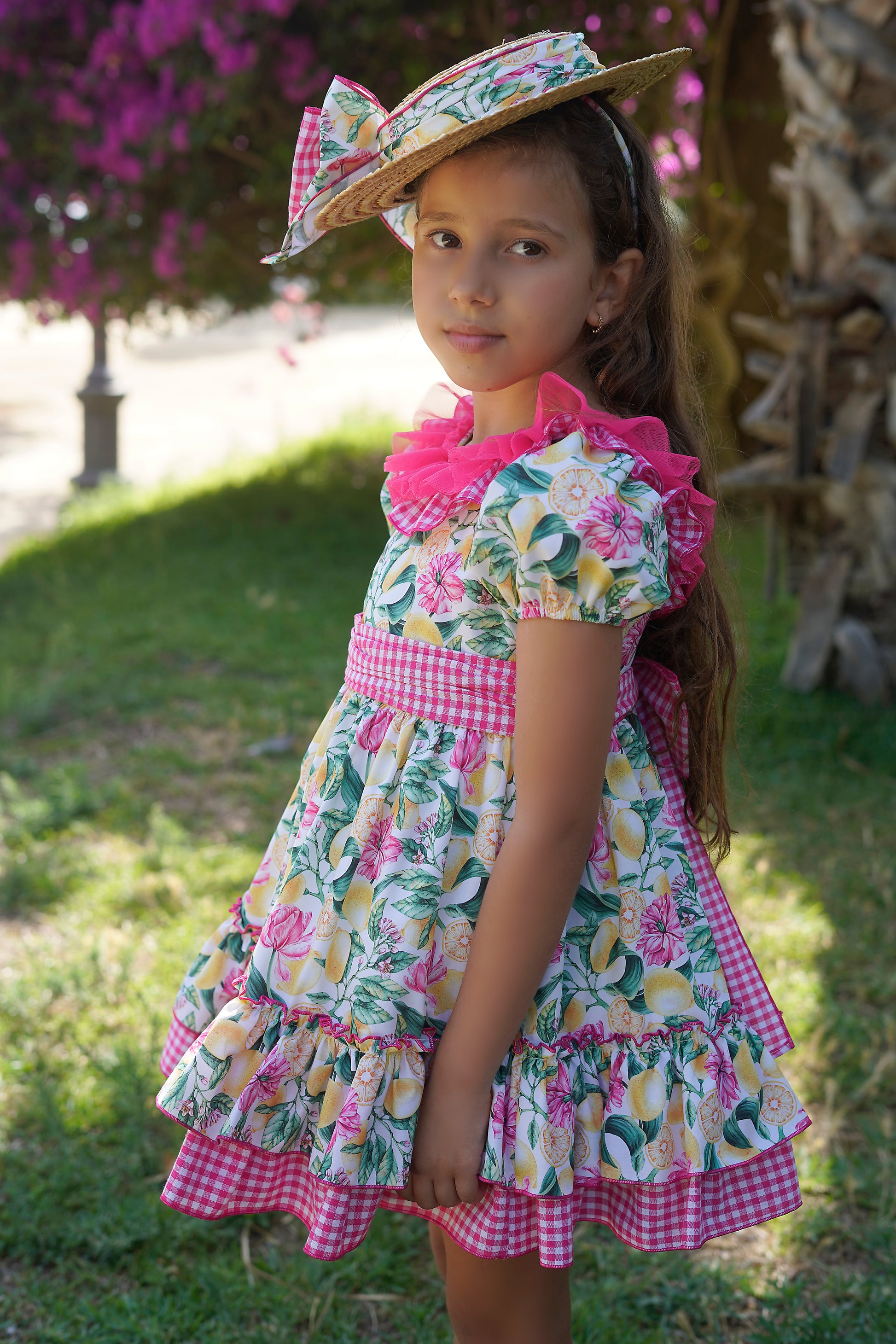 Young girl wearing a floral dress with ruffles and a matching hat outdoors.
